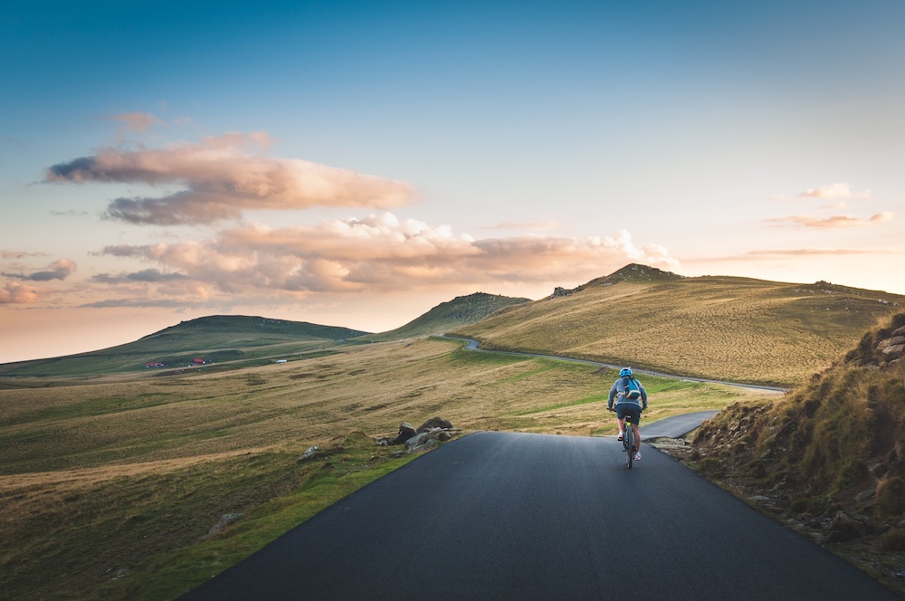 A cyclist riding on a road along grassy hills